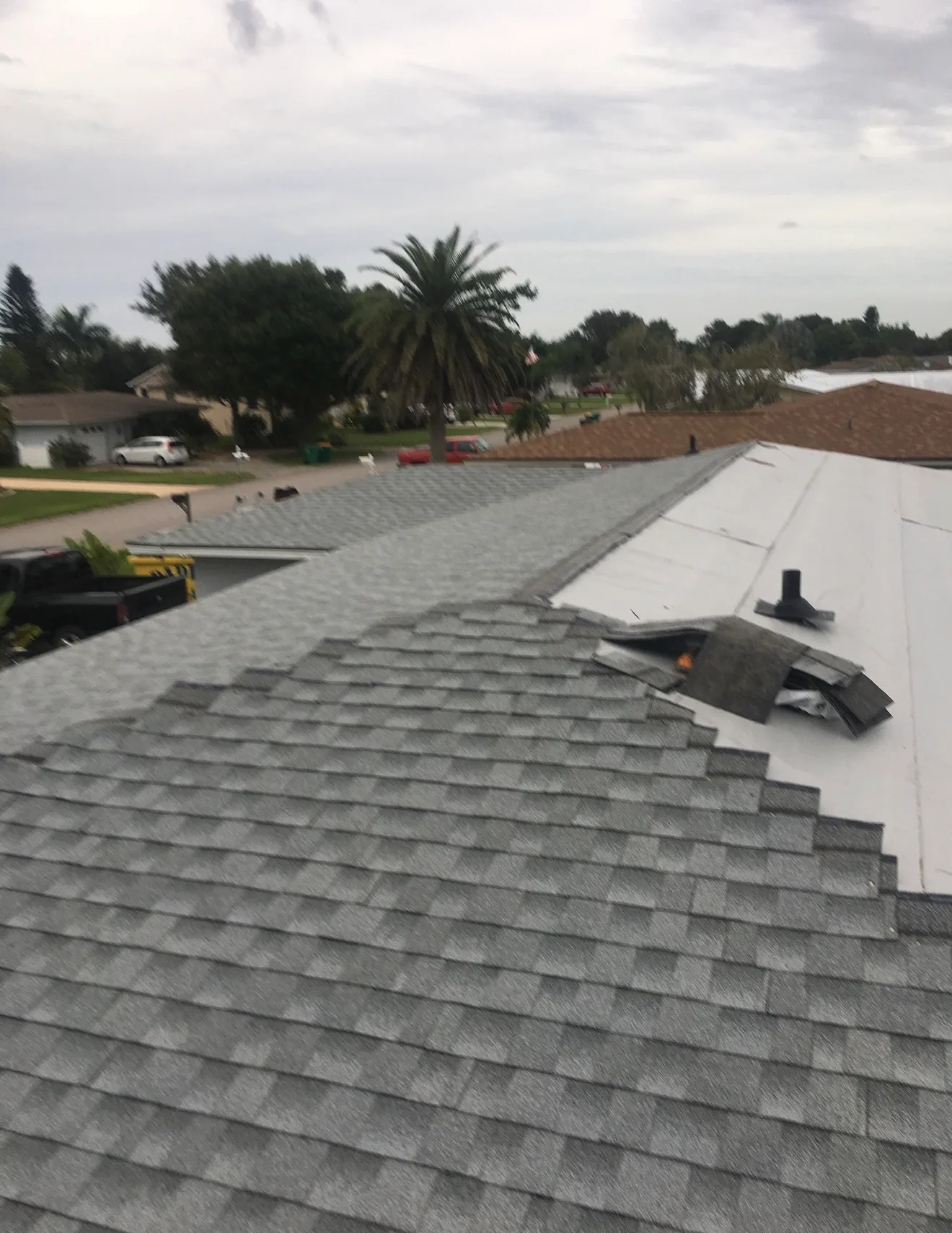 Shingle roof repair work in progress showing gray asphalt shingles with installation materials and tools on residential roof