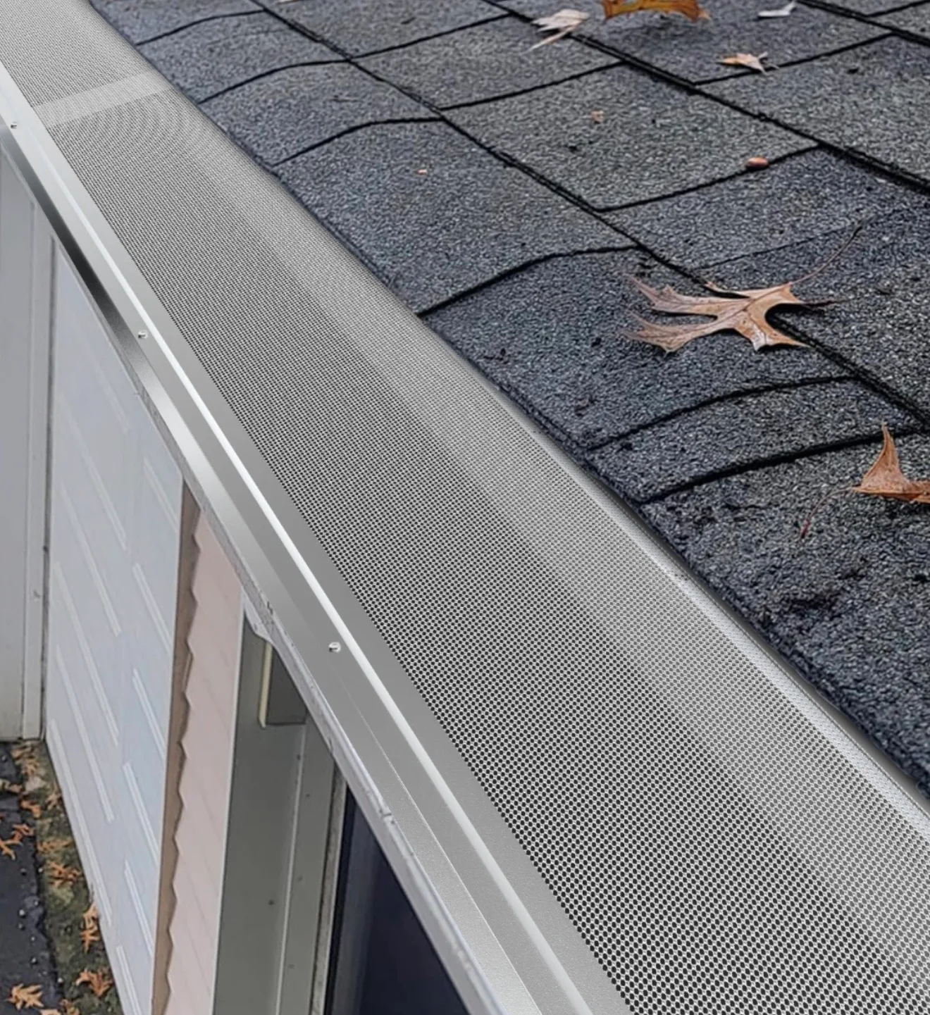 Asphalt shingle roof with white gutters, fascia, and fall leaves on residential roofing surface