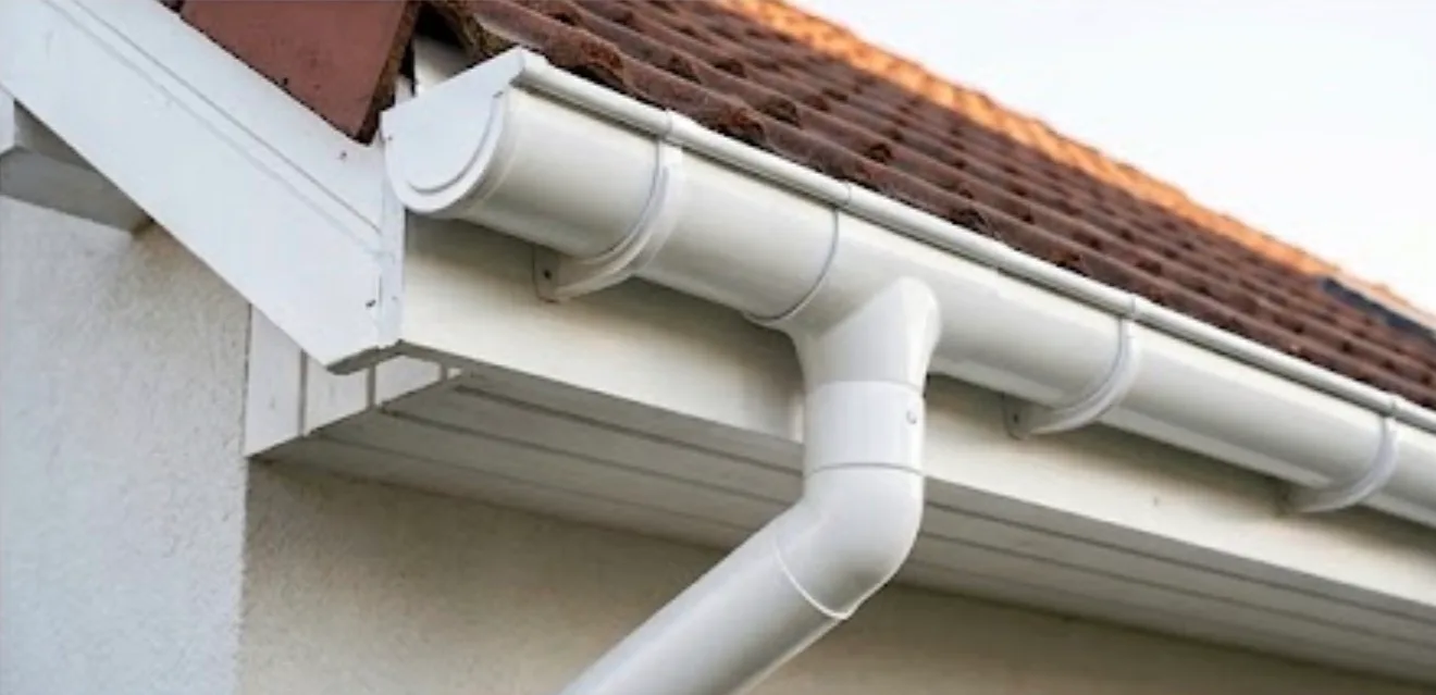 White seamless gutter system with downspout installed on residential roof edge