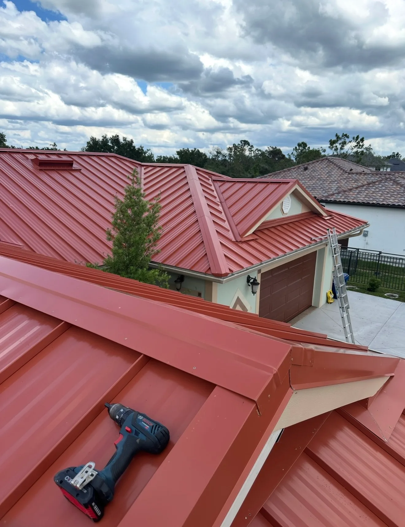 Newly installed red standing seam metal roof showing completed metallic roofing system with work in progress