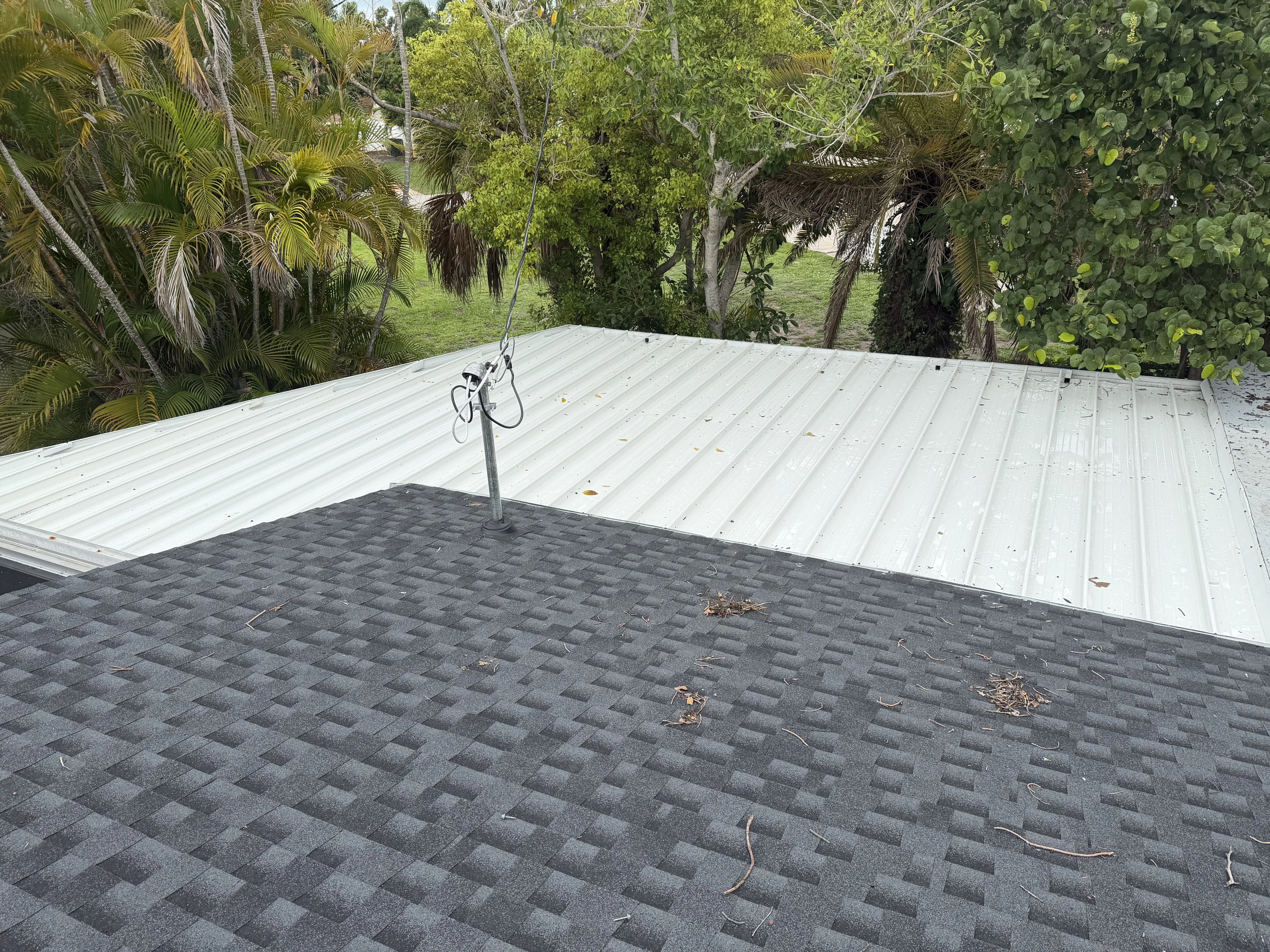 Completed roof with gray asphalt shingles on left and white standing seam metal roof on right