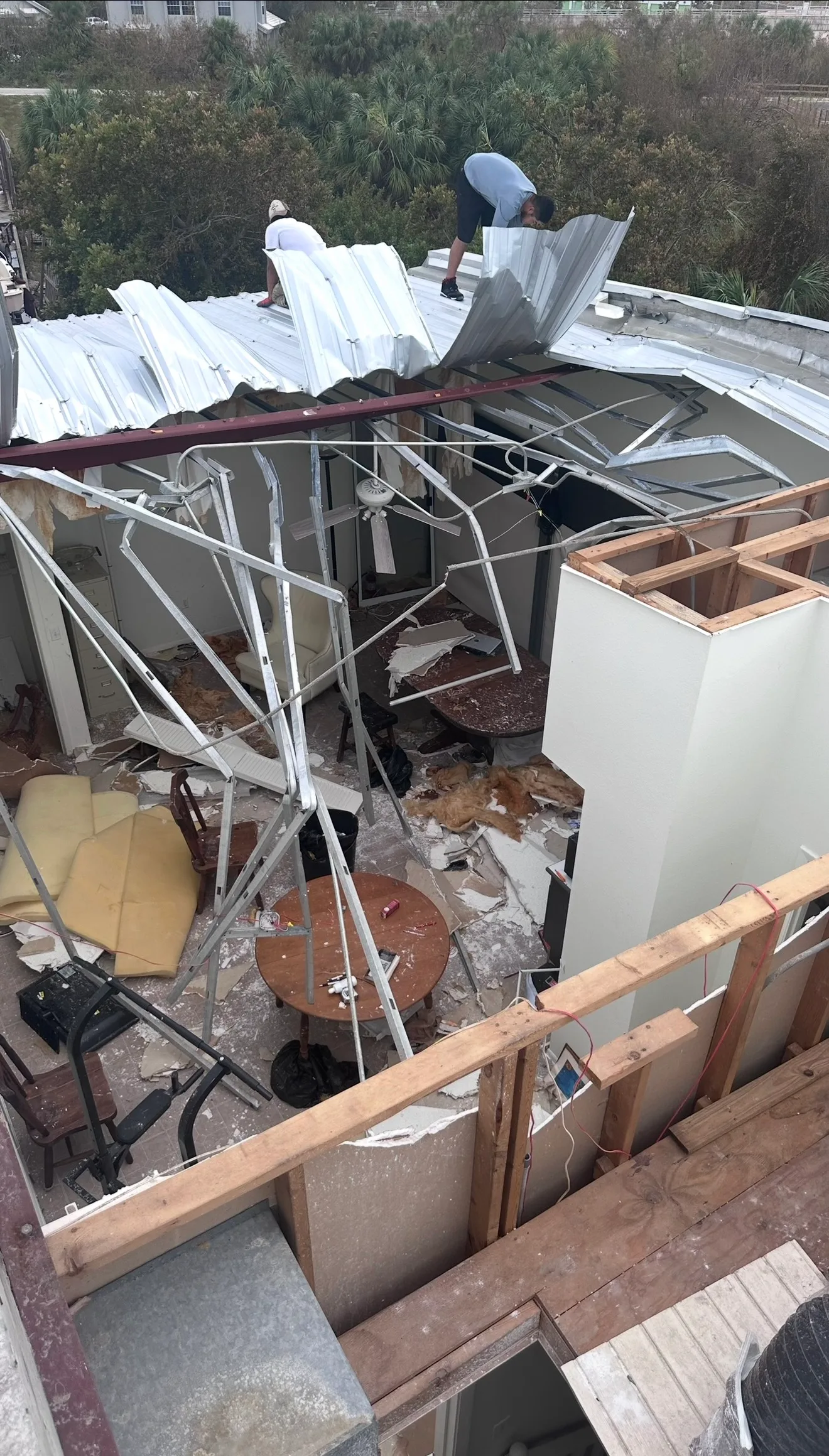 Storm-damaged residential roof with exposed framing and scattered roofing materials