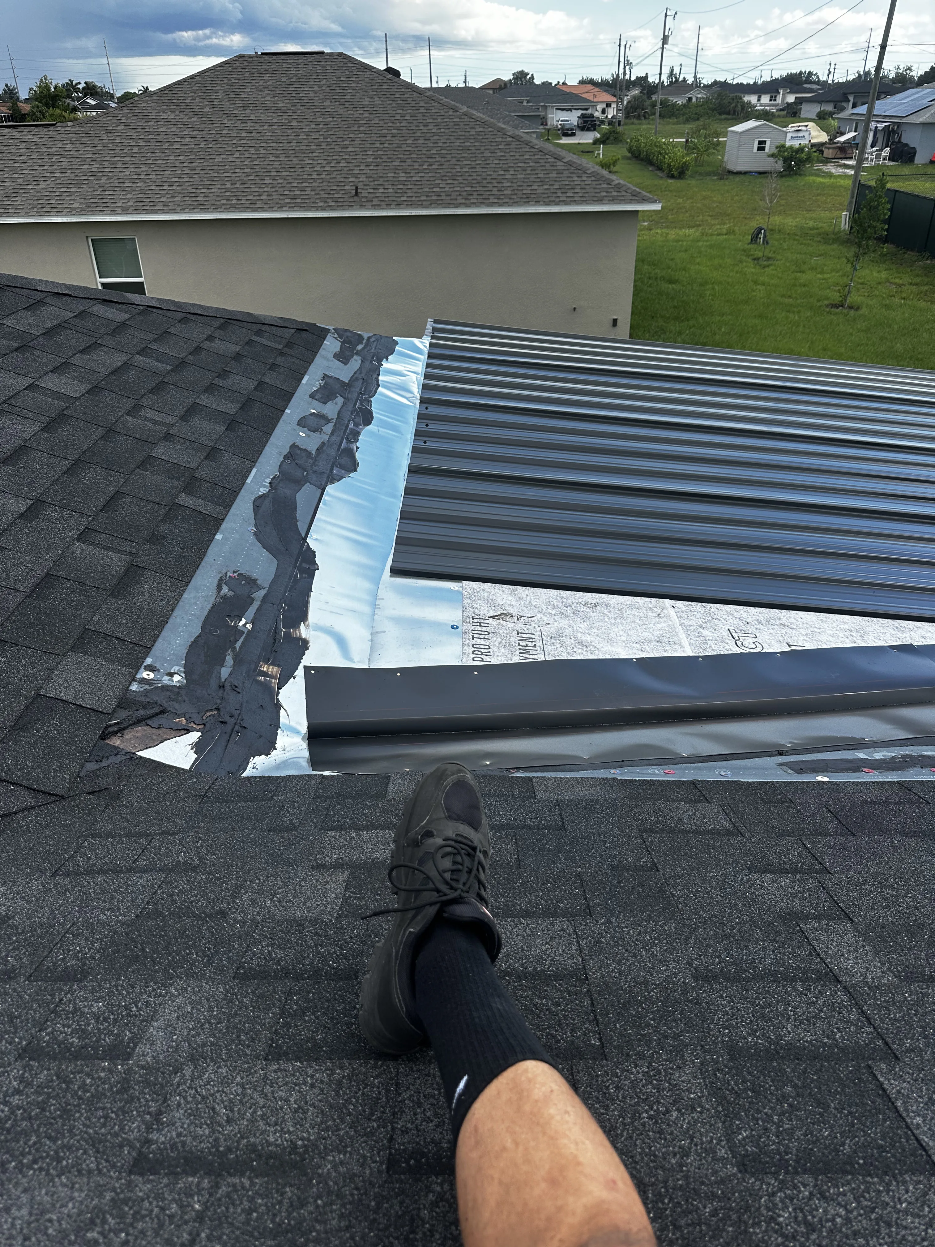 Metal roof replacement showing standing seam metal panels installed on residential roof next to existing shingles