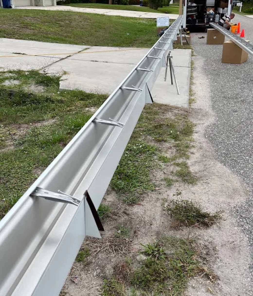 Seamless aluminum gutter installation running along residential home exterior during construction