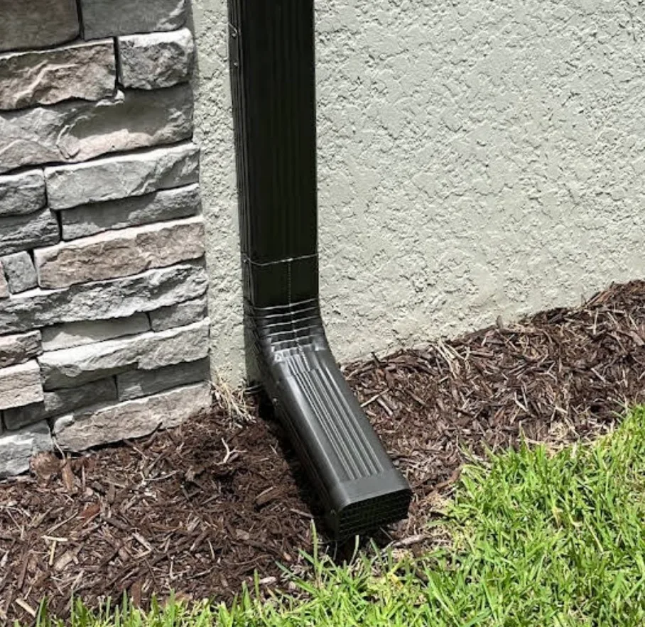 Black metal downspout gutter installation on white residential building exterior near stone wall