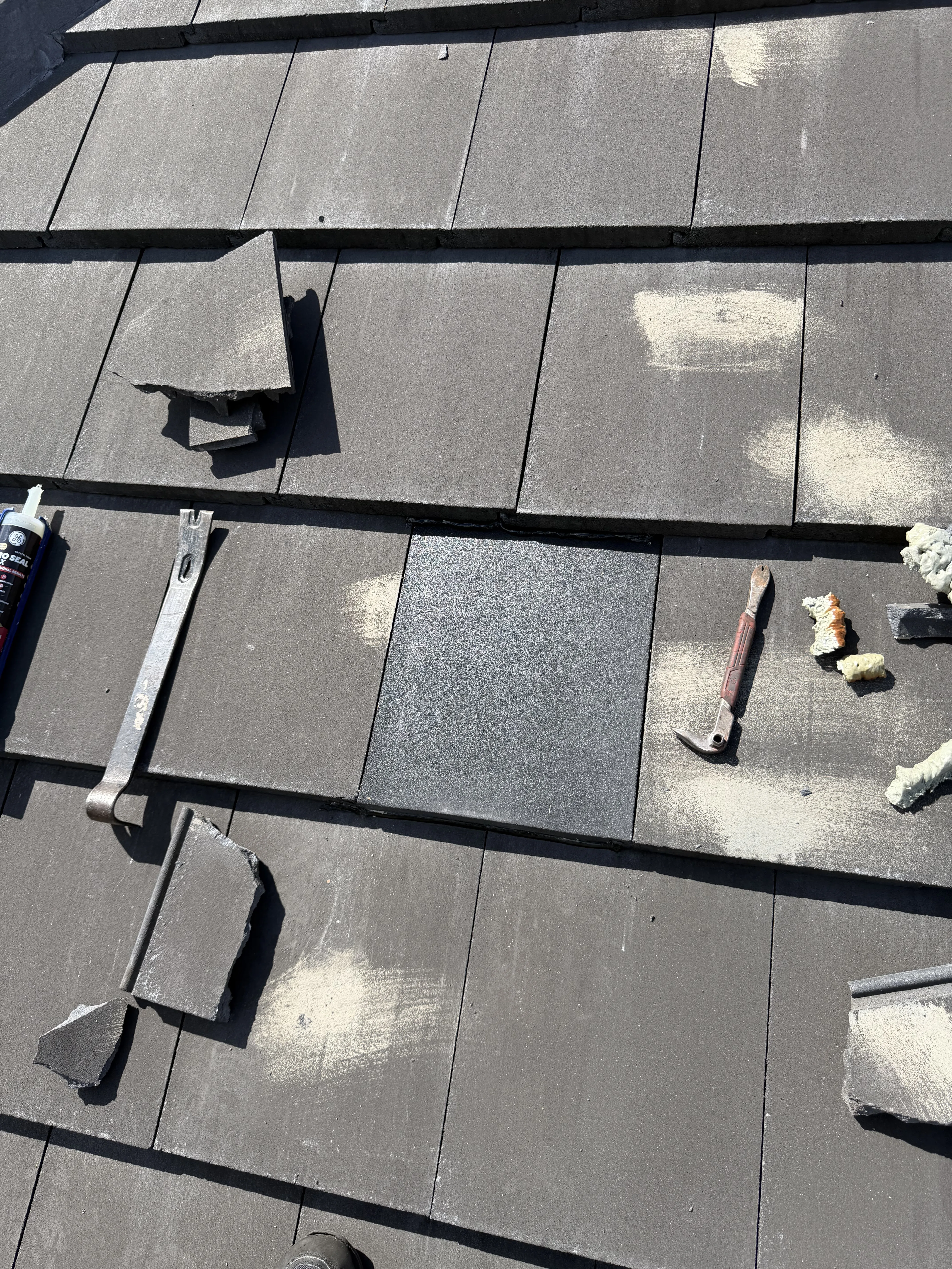 Standing seam metal roof installation showing gray metal panels with black seams and tools during roof work process