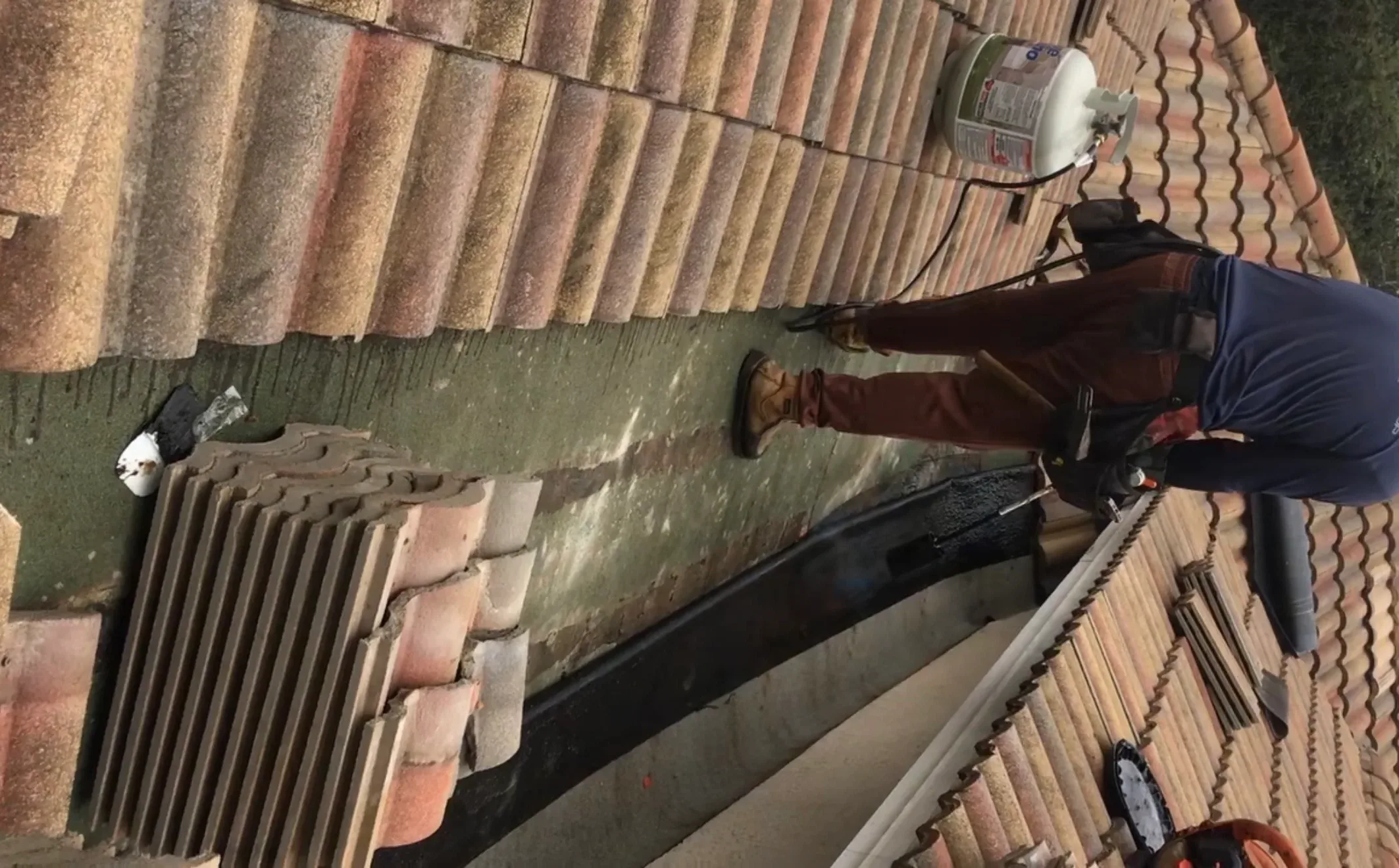 Professional roofer performing tile roof repair and maintenance work on residential clay tile roof