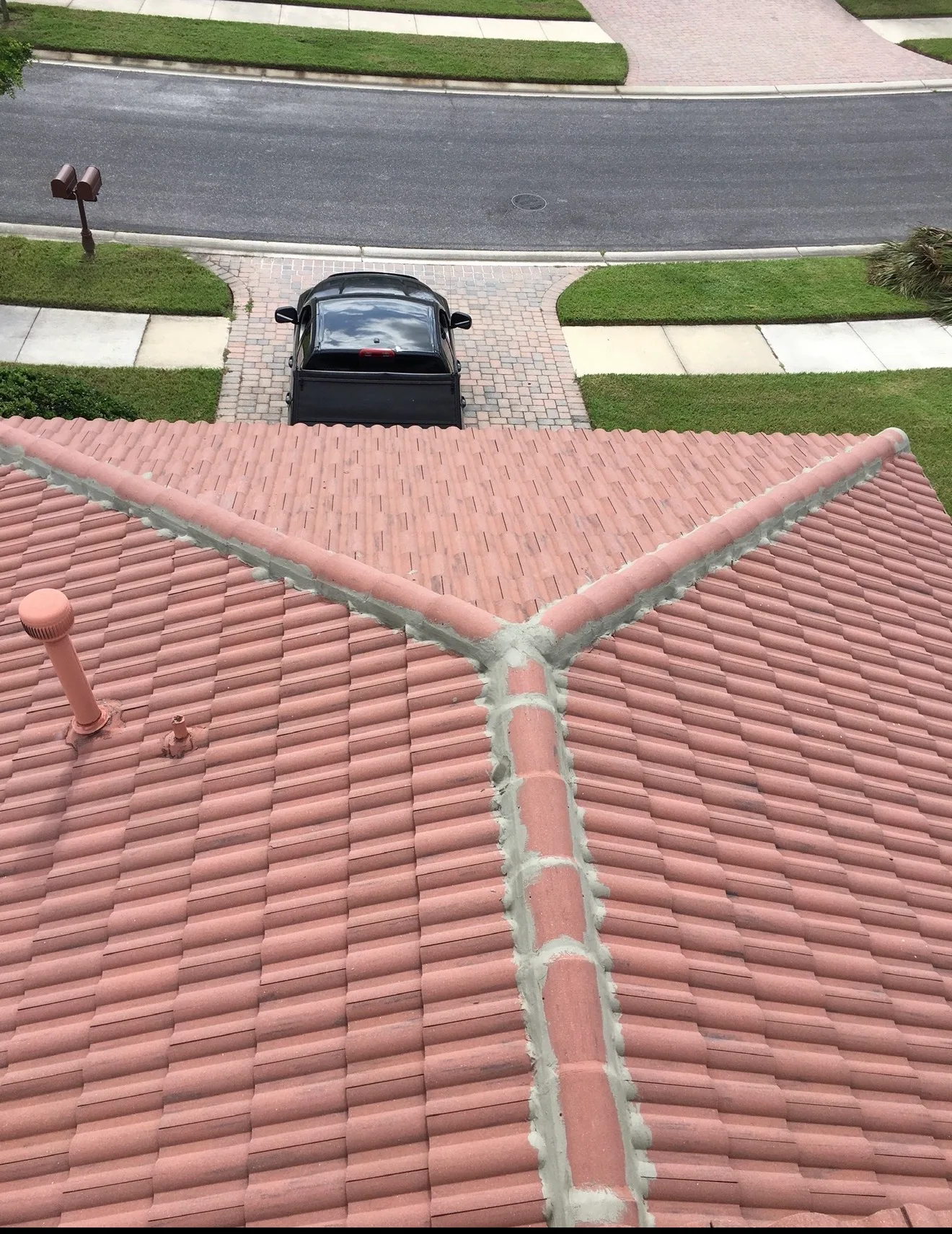 Red tile roof with fresh mortar seams, taken from rooftop showing driveway and residential property below