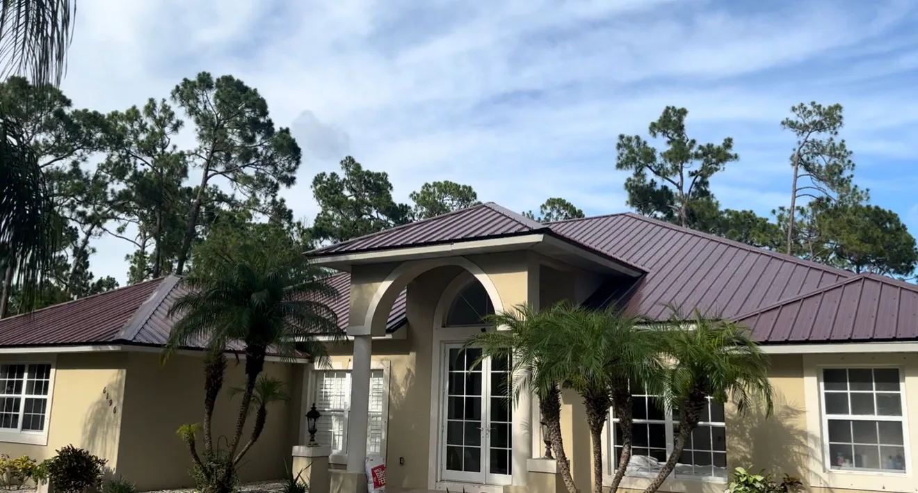Standing seam metal roof installation on residential home with tan stucco walls and palm landscaping