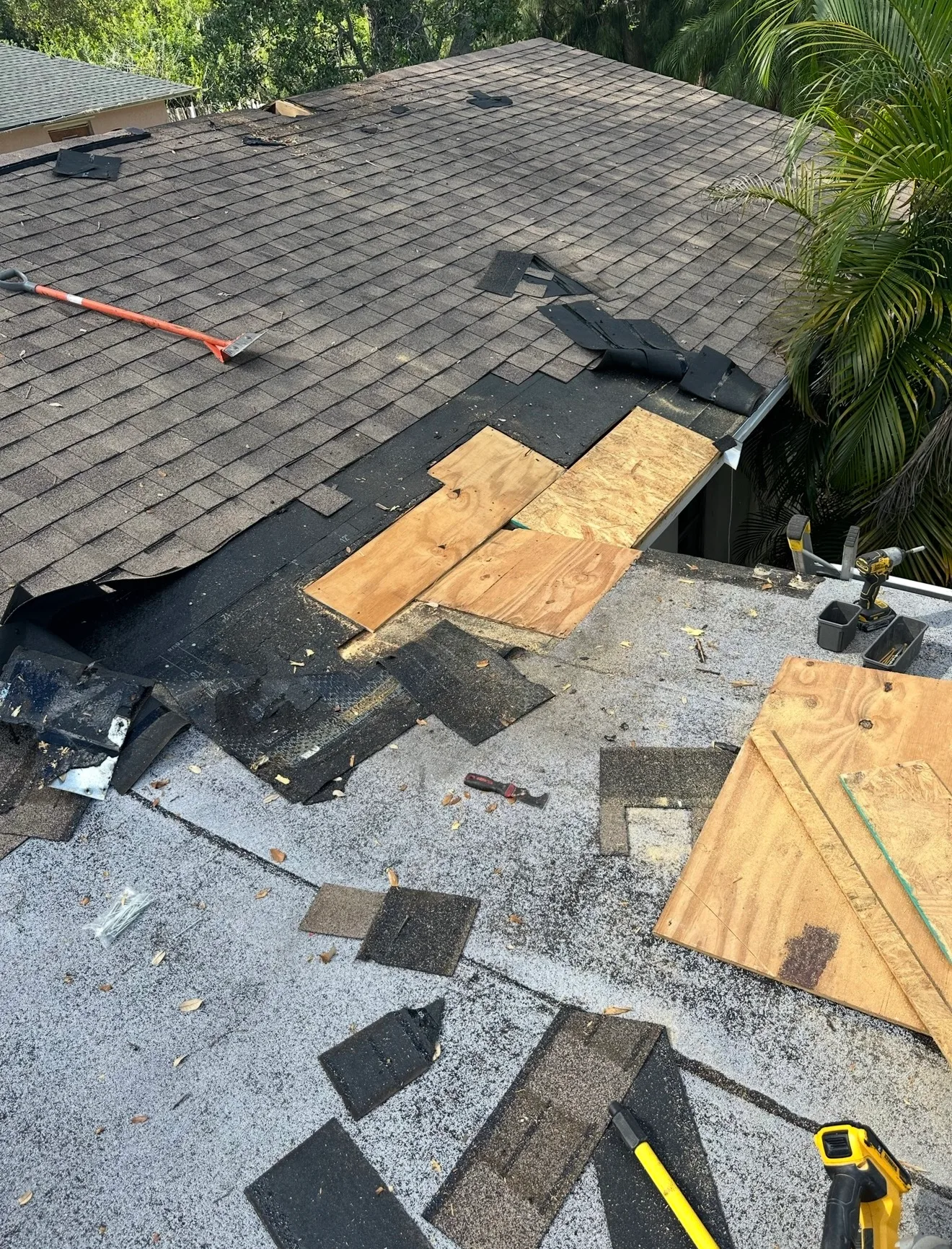 Shingle roof repair in progress showing damage patched with wooden plywood, surrounded by removed roofing materials and work tools