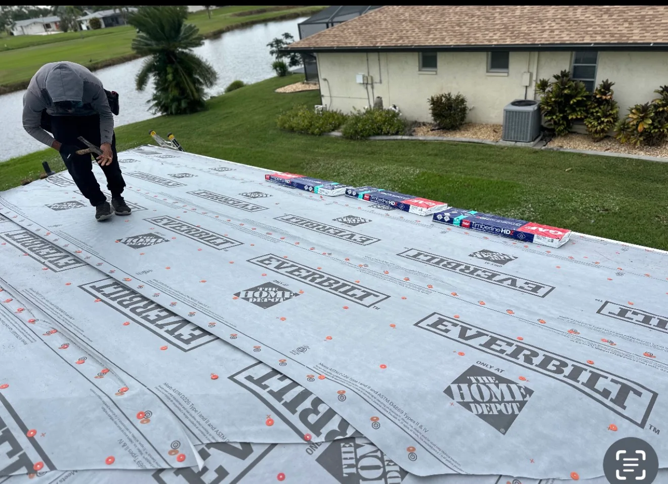 Roofer inspecting roofing underlayment materials and shingles laid out on residential property lawn for installation