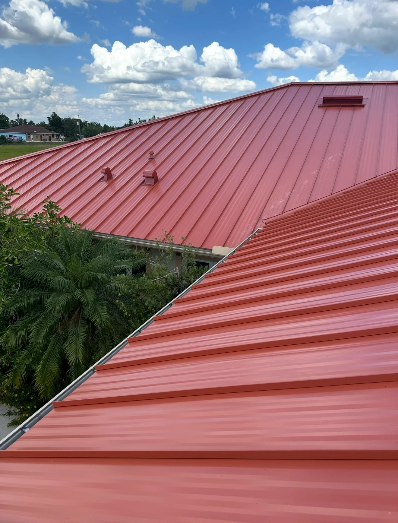 Standing seam metal roof with red vertical ribbed panels and roof vents