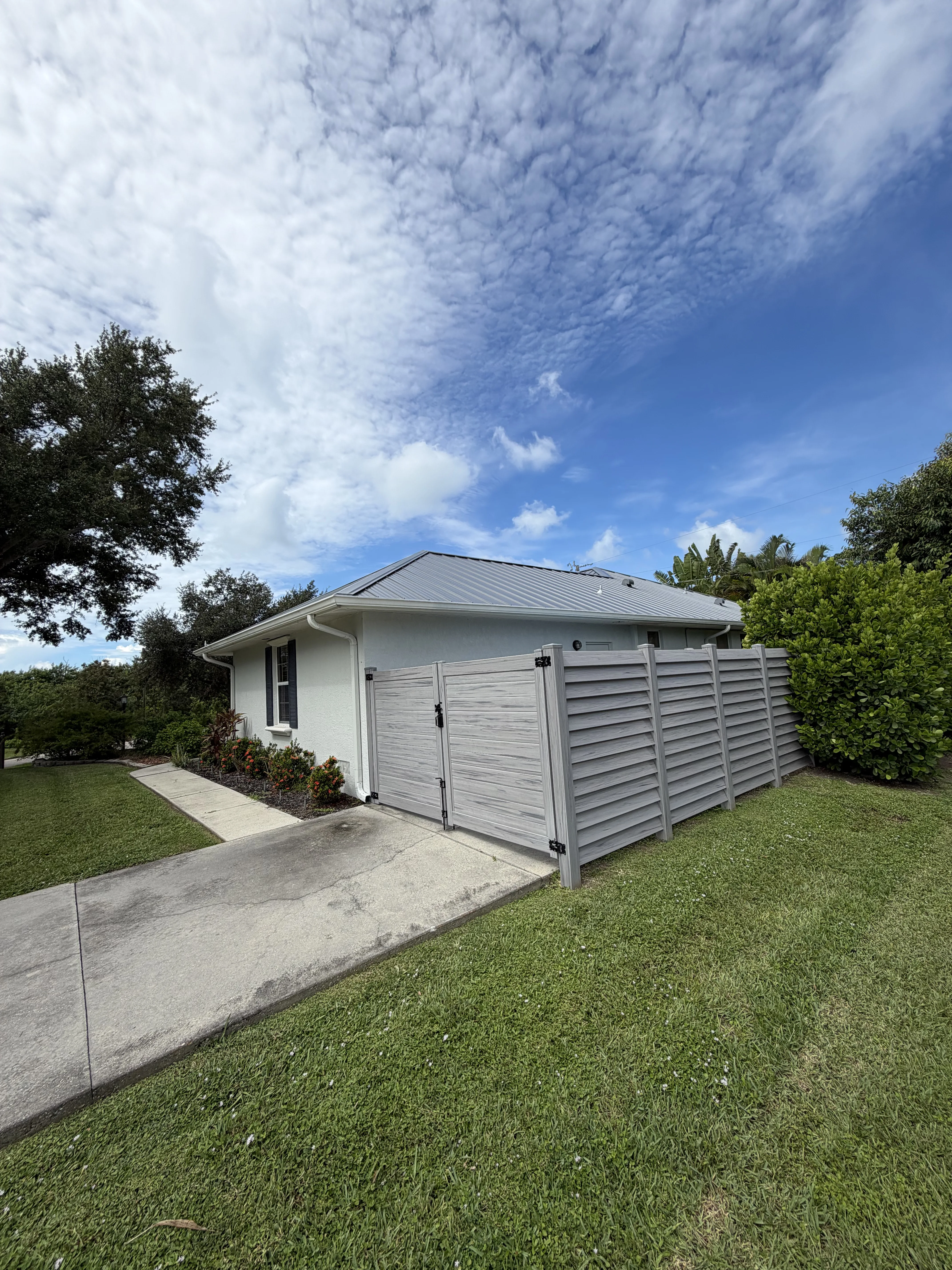 Standing seam metal roof installation on white residential garage with gray front doors and landscaped setting