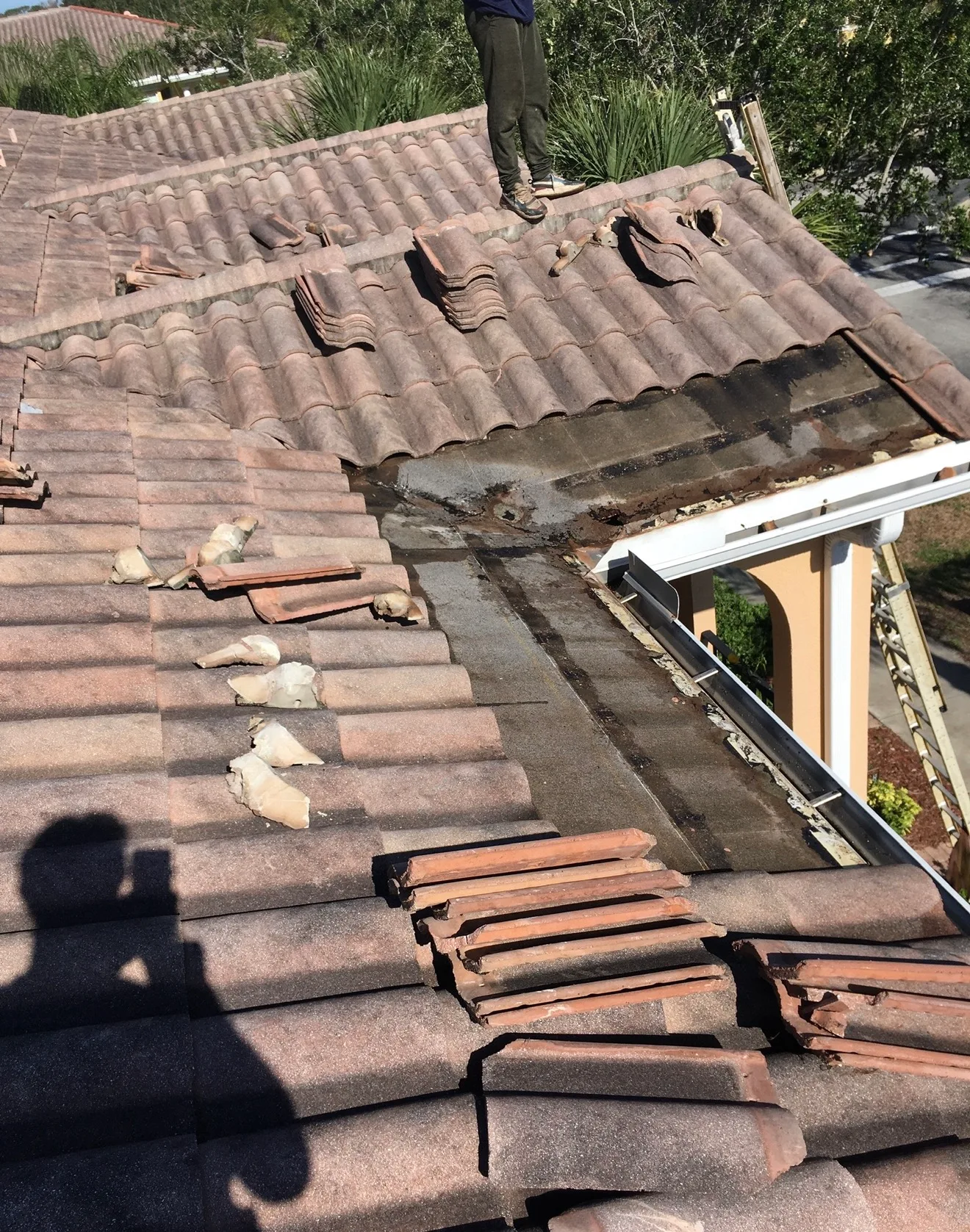 Roofer repairs damaged clay tile roof with broken tiles removed and replacement tiles stacked on roof surface