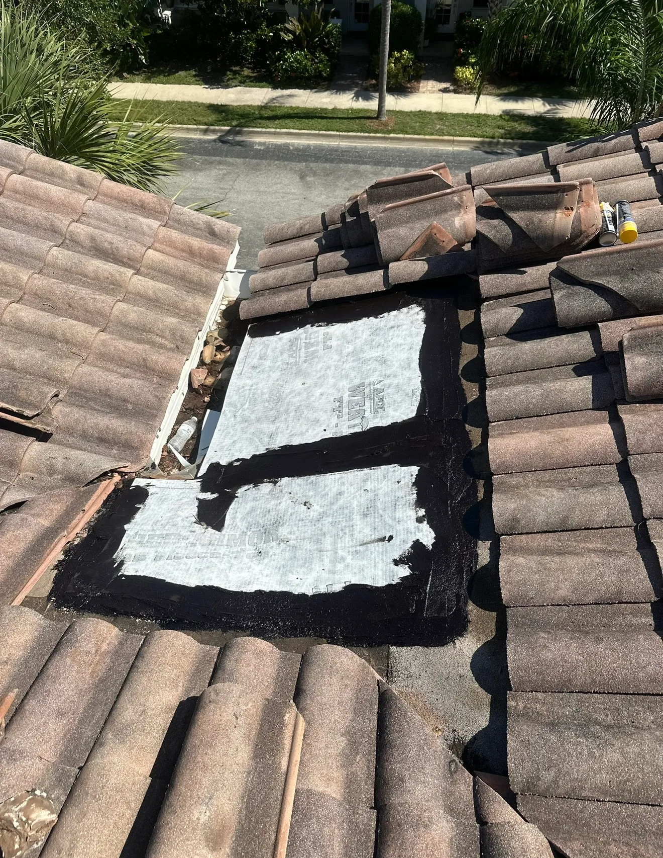 Tile roof repair showing damaged section with white underlayment exposed and dark waterproof membrane applied during restoration