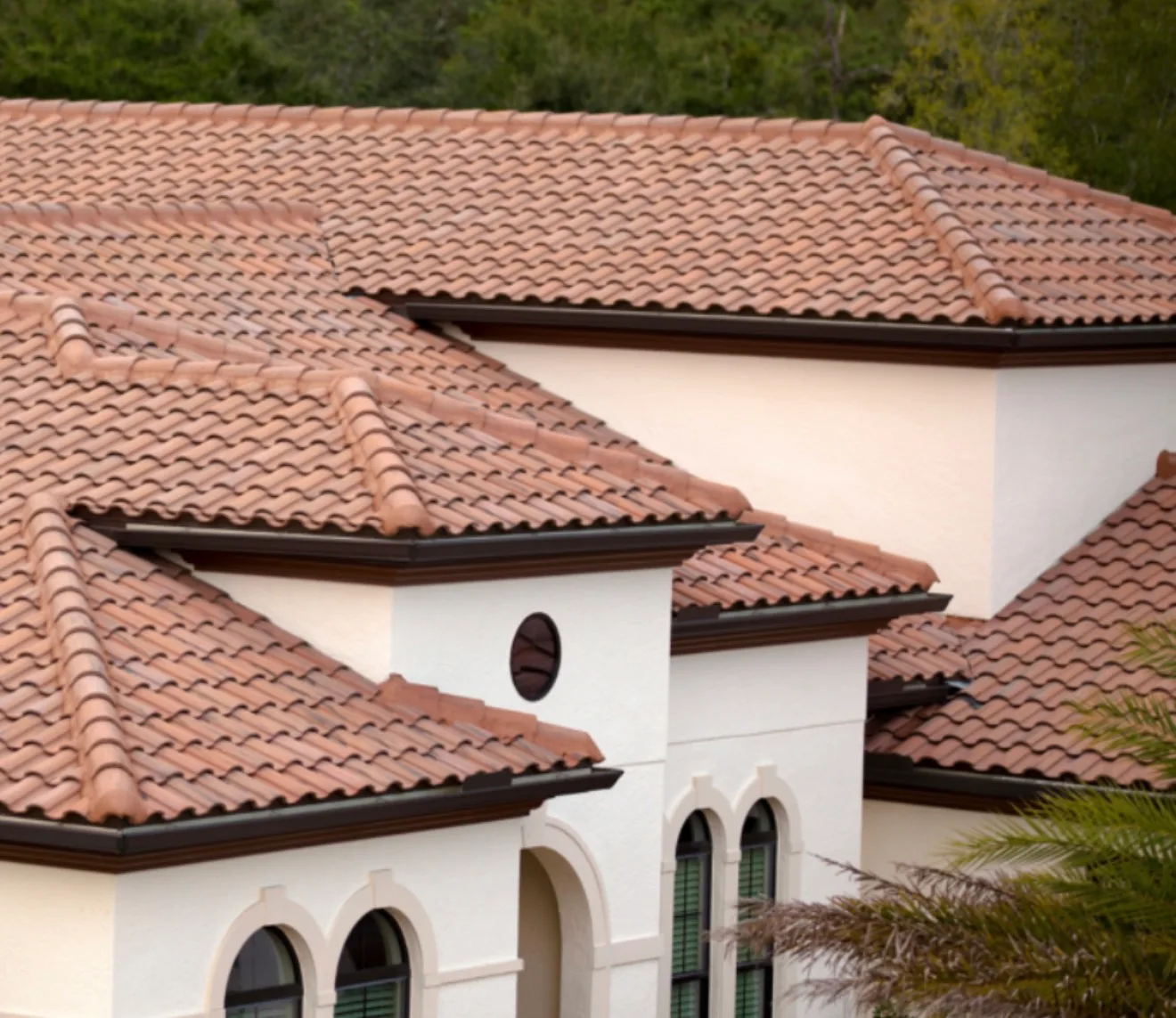Residential tile roof with terra-cotta clay tiles, white stucco walls, and arched windows on Spanish-style home